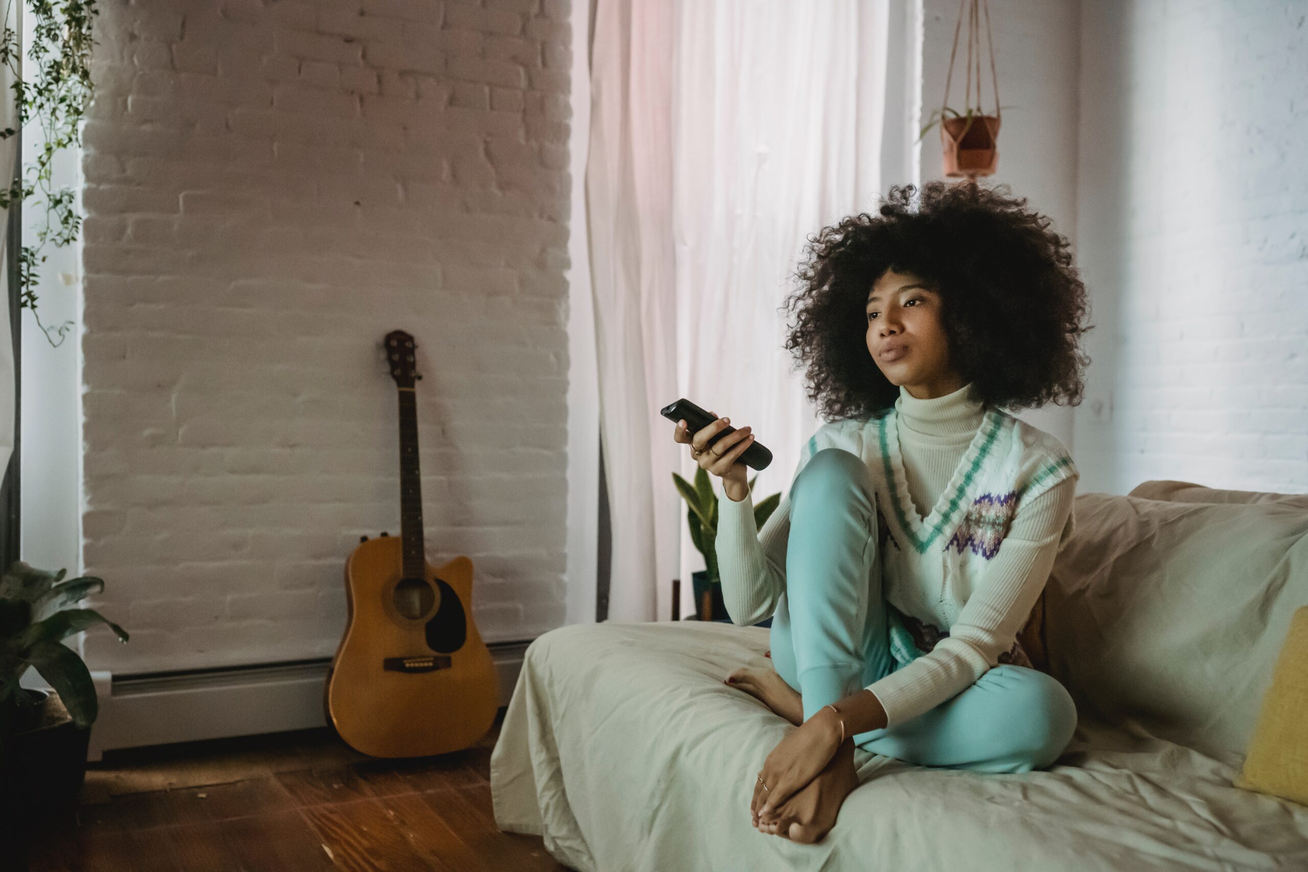 Jeune femme noire regardant sa télévision, télécommande à la maison sur son canapé